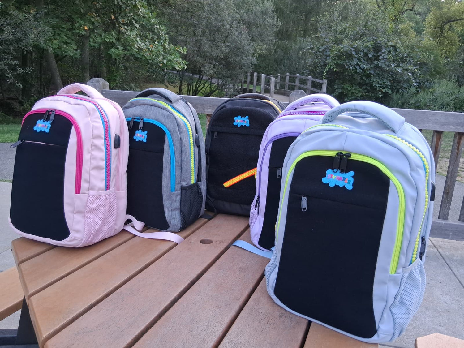 Five colorful backpacks on a wooden table outdoors.