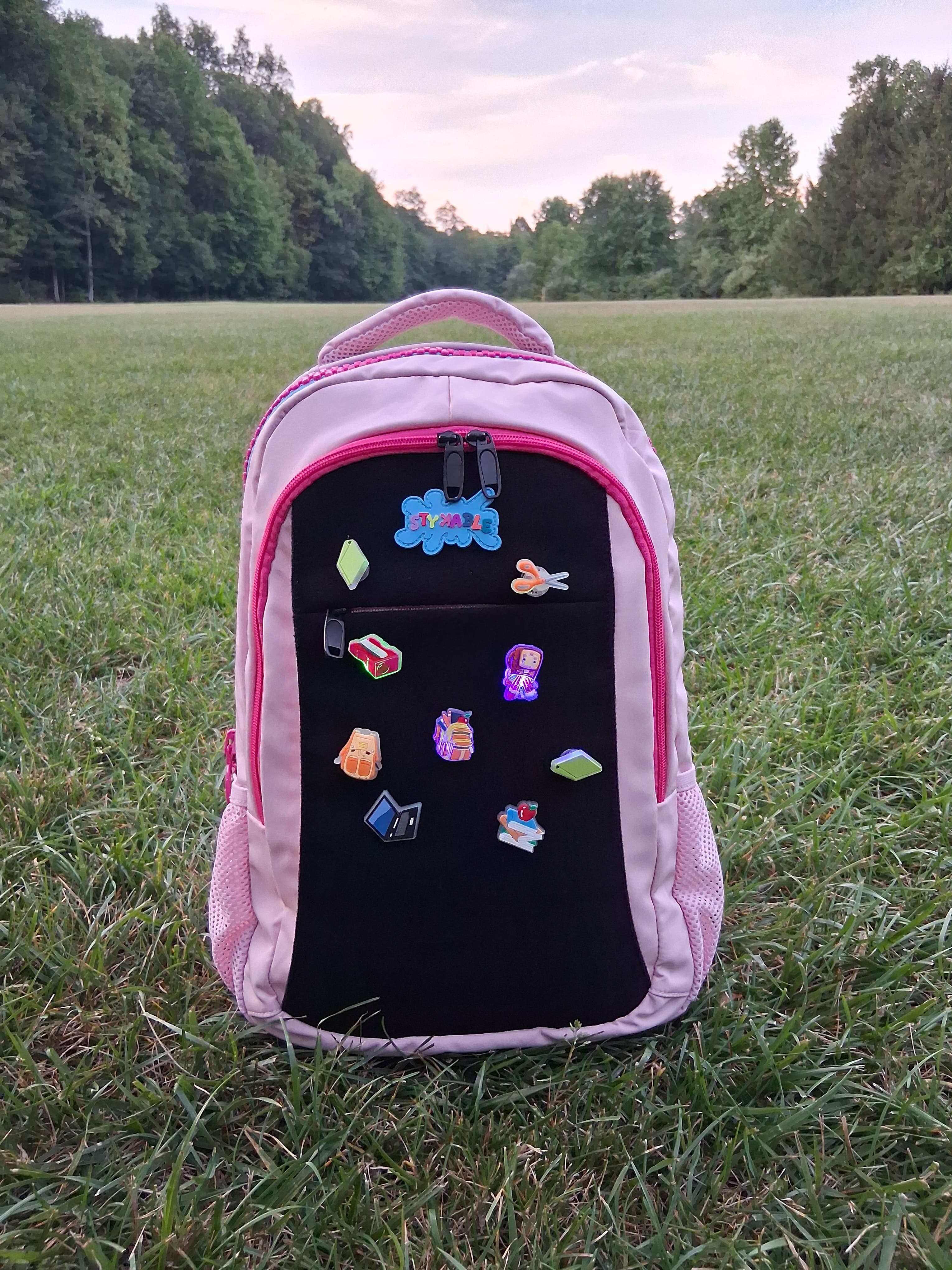 Pink backpack with colorful magnets on a grassy field